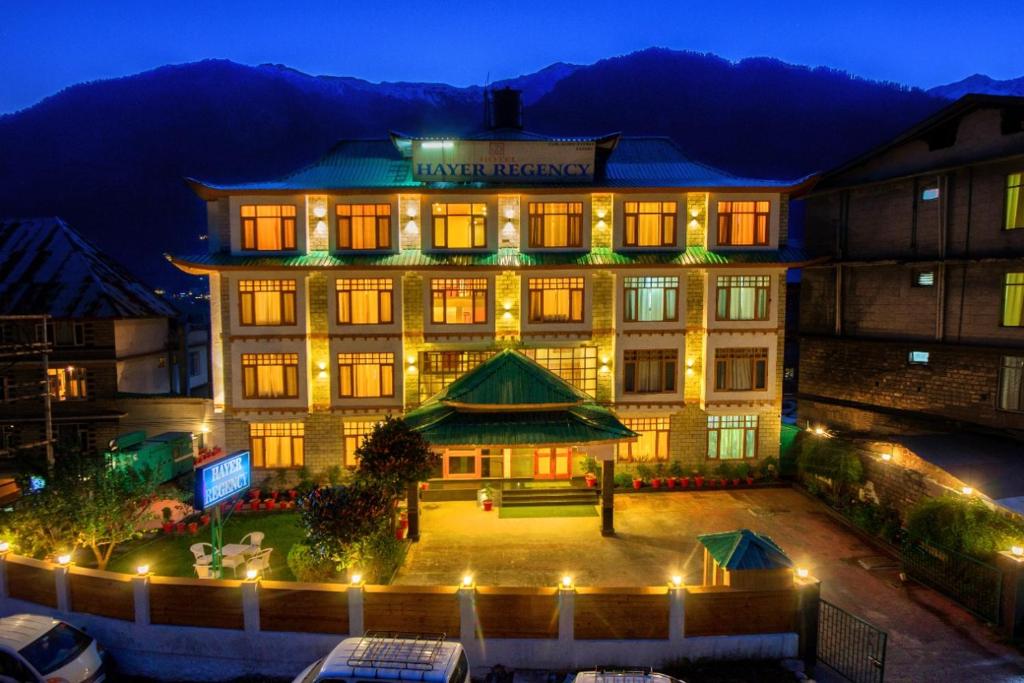 un grande edificio con luci di notte davanti di Hotel Hayer Regency a Manāli