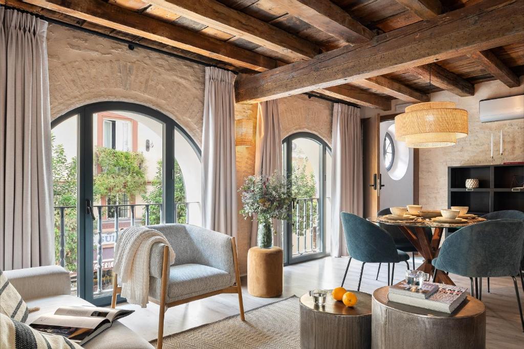 ein Wohnzimmer mit großen Fenstern sowie einem Tisch und Stühlen in der Unterkunft La Sillería de Arfe by Magno Apartments in Sevilla
