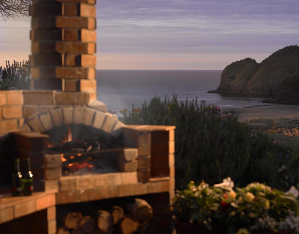 a stone fireplace with a view of the ocean at Bethells Beach Cottages in Bethells Beach