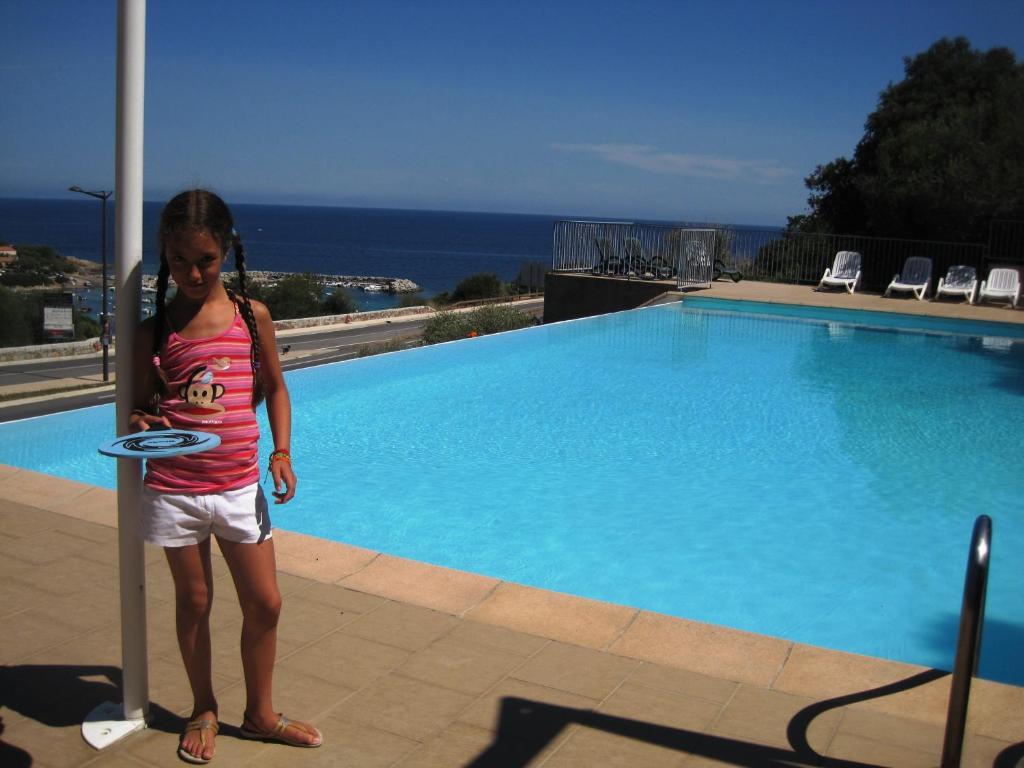 una ragazza in piedi accanto a una piscina con un frisbee di Residence San Damiano - Location Appartements, Studios & Chambres a Algajola
