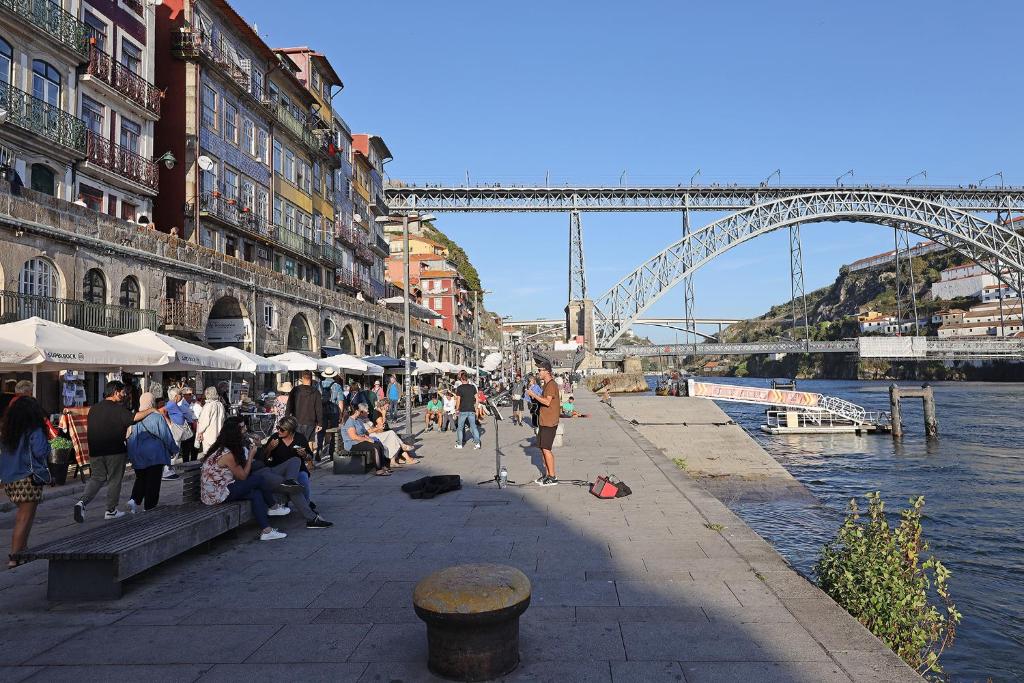 un grupo de personas sentadas en una acera cerca del agua con un puente en FLH Porto Ribeira with River View en Oporto