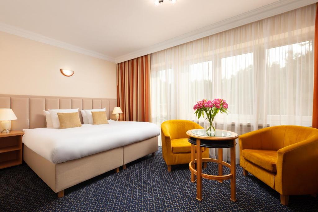 ナダジンにあるPerła Leśna Nadarzynのベッド、テーブル、椅子が備わるホテルルームです。