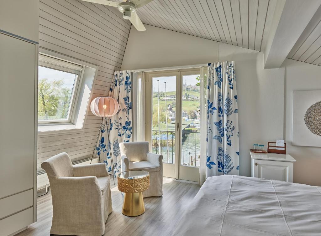 a bedroom with a bed and two chairs and a window at Strandhotel Schmerikon in Schmerikon