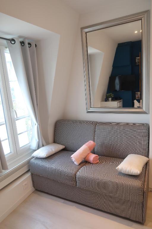 Sofá con 2 almohadas y espejo en Paris 17 - Batignolles - Studio 10 m2 - 1 room - Single occupancy - near Champs Elysées & Montmartre & Dpt stores, en París