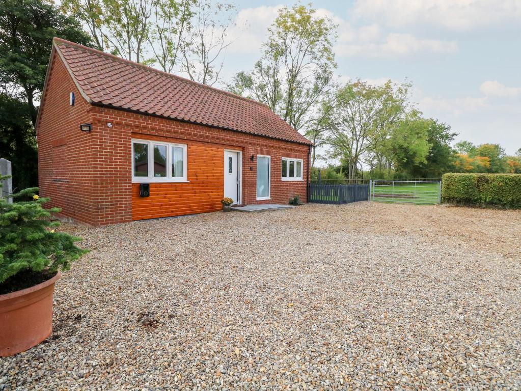 a small red brick house on a gravel driveway at Robin's Nest in Brisley