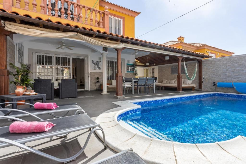 einen Pool in einem Garten mit Stühlen und einem Haus in der Unterkunft LUXURY VILLA WITH PRIVATE POOL WITH AIRCON,Playa del Duque in Adeje