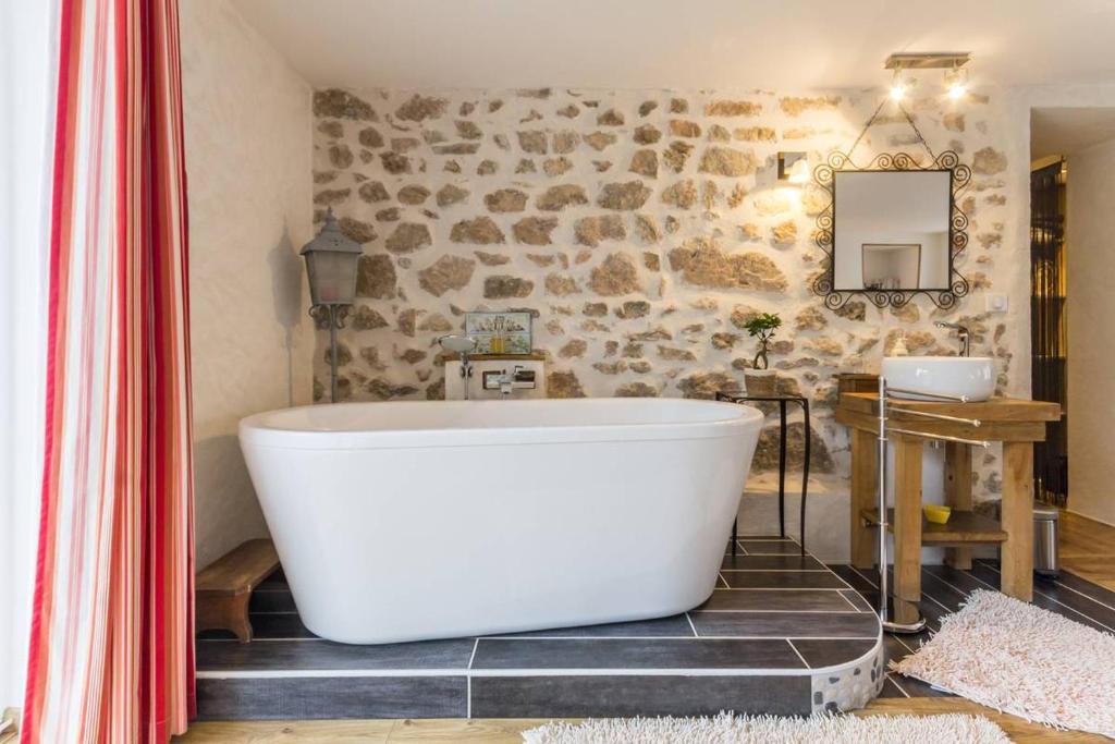 y baño con bañera grande y pared de piedra. en L'Escale du Banquet, en Mhère