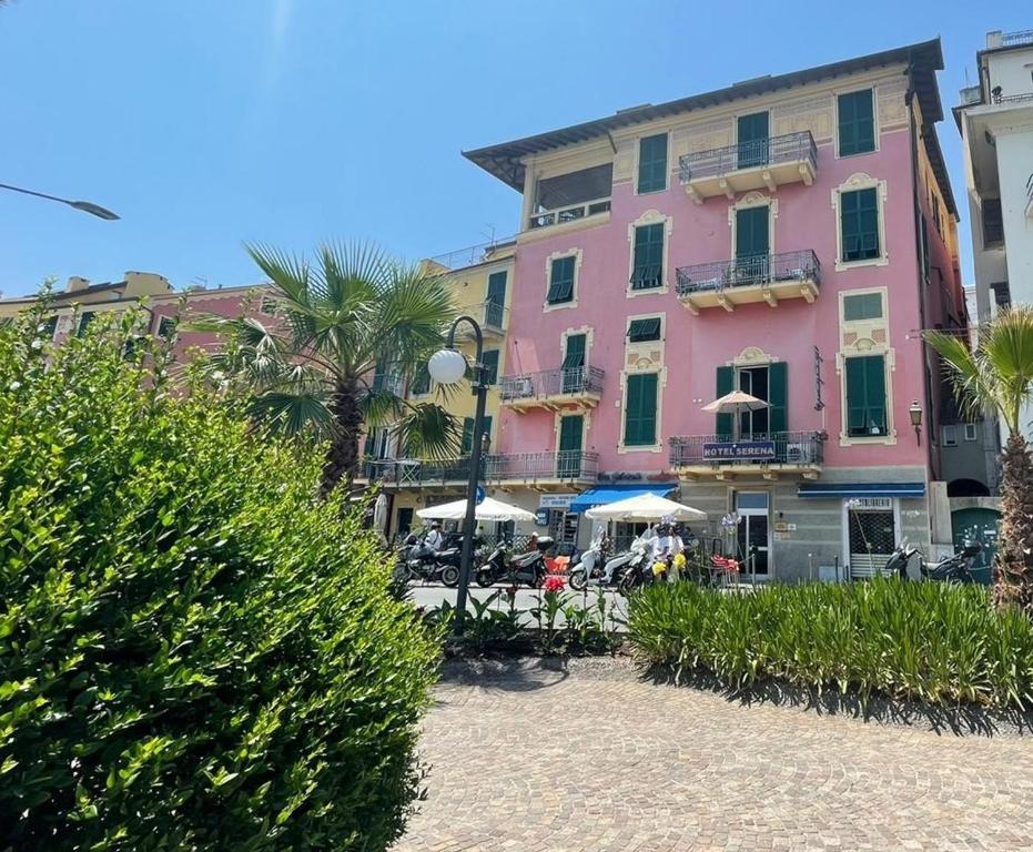 un edificio rosa con tavoli e ombrelloni di fronte di Hotel Serena ad Arenzano