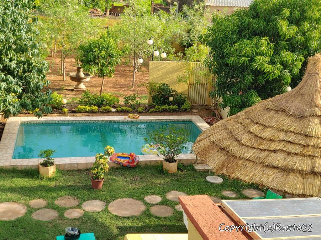 un patio trasero con piscina y sombrilla de paja en Résidence des hibiscus-roses: jardin, piscine..., en Ouagadougou