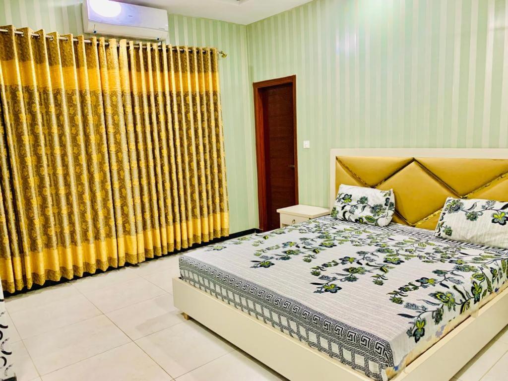 a bedroom with a large bed and yellow curtains at The Crown in Islamabad