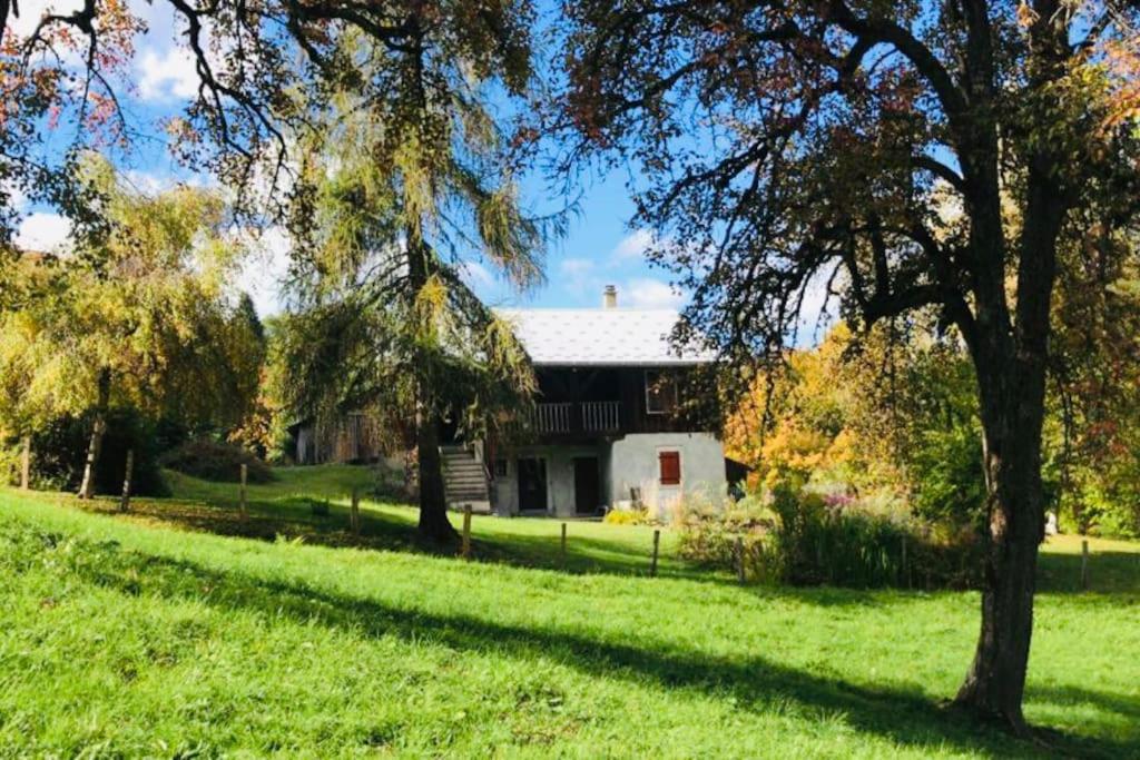 ein Haus auf einem grünen Feld mit Bäumen im Vordergrund in der Unterkunft Le Chalet de Bémont in Samoëns