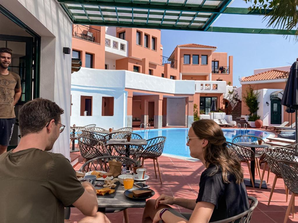 a man and woman sitting at a table near a pool at Nisea Hotel Samos in Pythagoreio