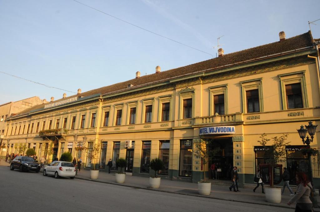 een gebouw in een straat waar auto's voor geparkeerd staan bij Hotel Vojvodina in Novi Sad