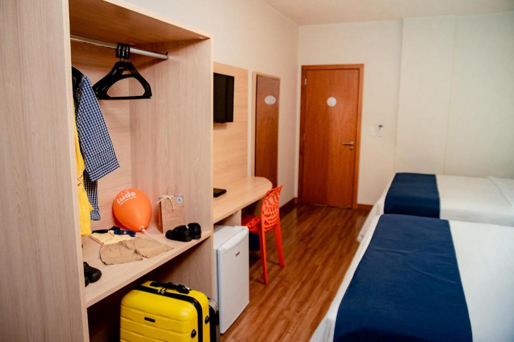 - une chambre avec un lit et un bureau avec une valise jaune dans l'établissement Luds Comfort Hotel, à Ponta Grossa