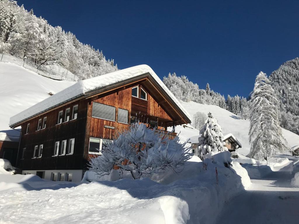 eine Holzhütte im Schnee mit schneebedeckten Bäumen in der Unterkunft Ferienwohnungen Lingg in Schoppernau