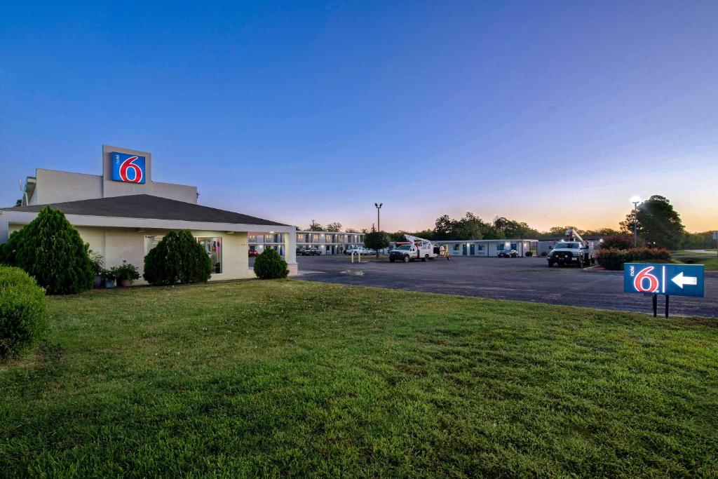 ein Gebäude mit einem Parkplatz mit einem Schild im Gras in der Unterkunft Motel 6-Sulphur Springs, TX in Sulphur Springs