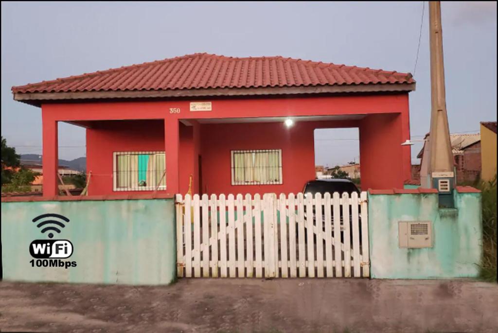 uma casa vermelha com uma cerca branca à frente. em Casa Pestana - Ilha Comprida em Ilha Comprida