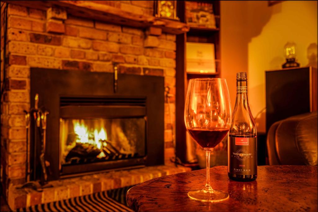 a glass of wine sitting on a table in front of a fireplace at Falls Lodge - a Blue Mountains experience in Wentworth Falls