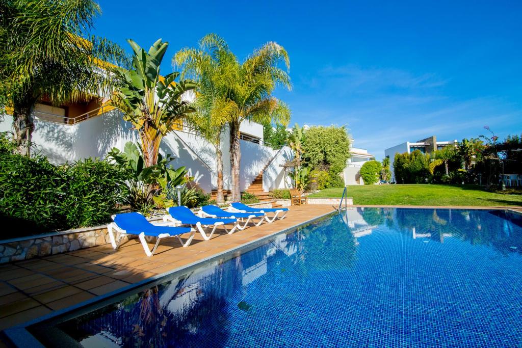 a swimming pool with blue chairs and a house at Pine Tree Apartments - Praia da Coelha - Albufeira in Albufeira