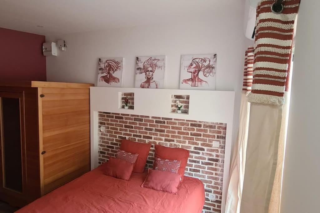 a bedroom with a red bed and a brick wall at Charmant studio climatisé avec Sauna in Le Bois de Nèfles