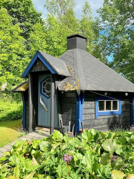 a small house with a blue door in a garden at StugaNäraKungsberget - mysig stuga med kamin, grillkåta och vedbastu in Ockelbo