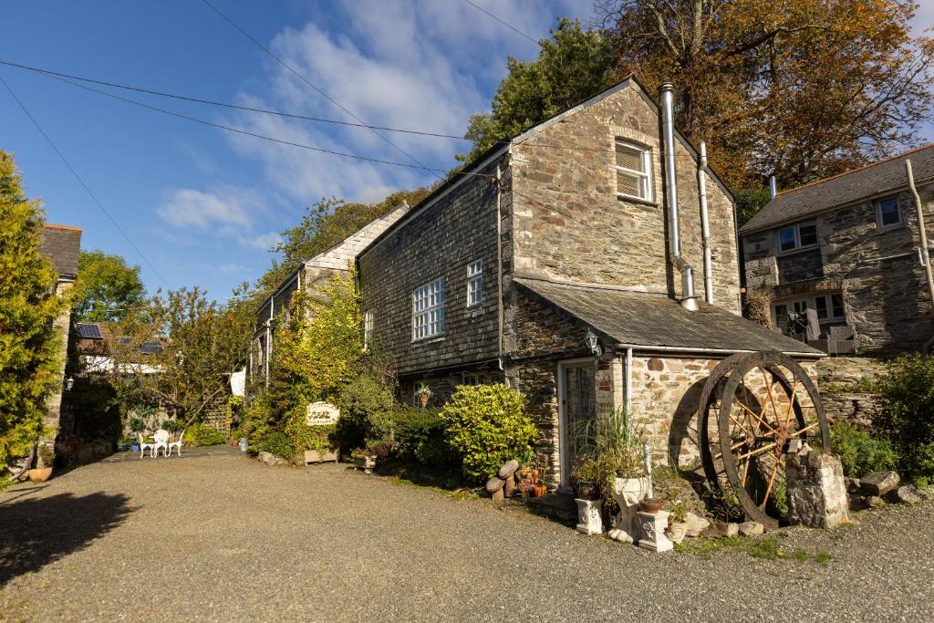 an old stone house with a large wheel in front of it at The Granary at Bissick Old Mill in Truro