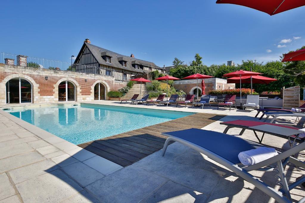 a swimming pool with chairs and umbrellas next to a building at Le Clos Des Fontaines in Jumièges