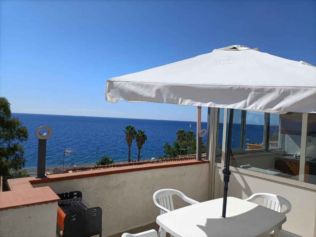 Biały stół i parasol na balkonie z widokiem na ocean w obiekcie Casa Vacanza Arcobaleno w mieście Ali Terme
