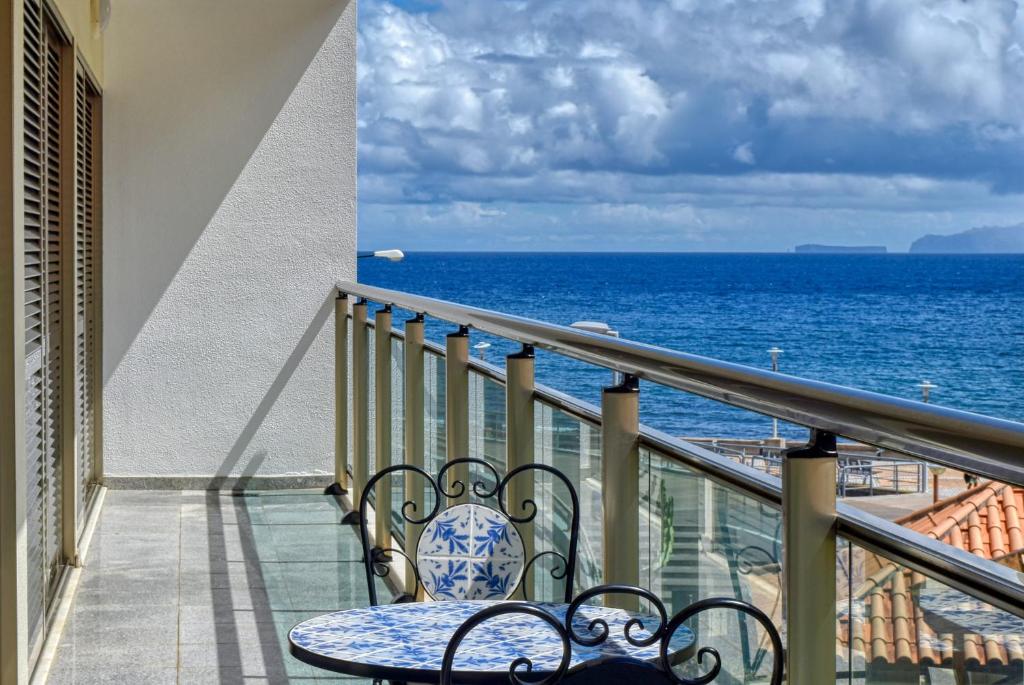 uma varanda com uma mesa e cadeiras e o oceano em Machico Beach, a Home in Madeira em Machico