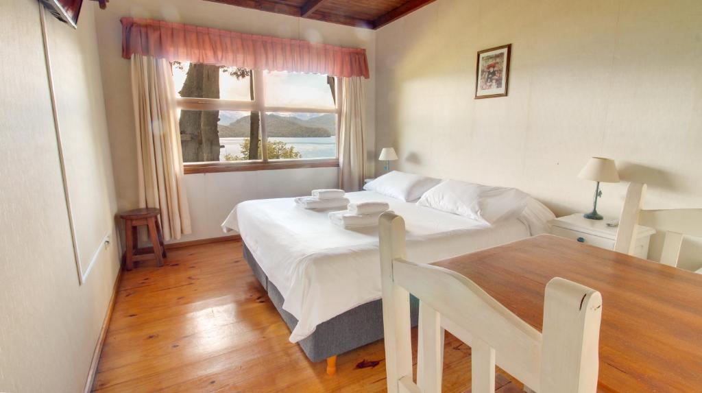 1 dormitorio con cama, mesa y ventana en Hosteria Belvedere en Villa La Angostura