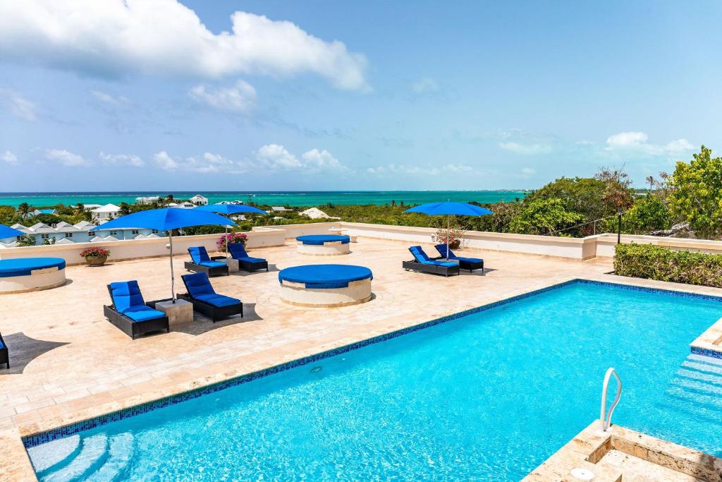 a swimming pool with chairs and umbrellas and the ocean at Sea Esta Studio I - Ideal for Couples! in Turtle Cove