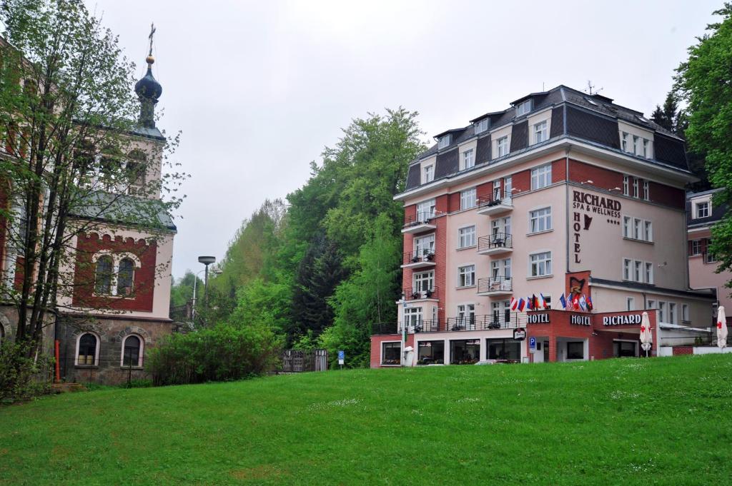 a building on a hill next to a green field at Hotel Richard Spa & Wellness in Mariánské Lázně