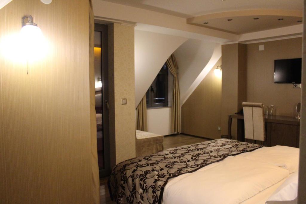Attic-style room with sloped ceiling, patterned bed runner, wall sconce, desk with kettle and bottled water, wall TV at City Palace Hotel in Ohrid