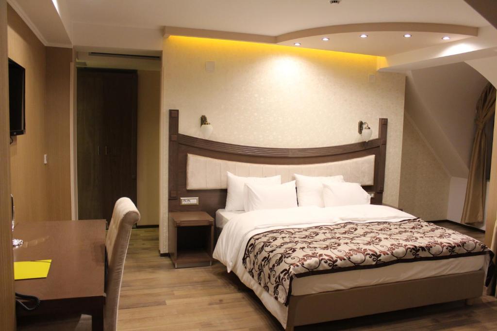 Double bed with patterned runner, wall sconces, bedside table with power outlets, desk with chair and wall-mounted TV at City Palace Hotel in Ohrid