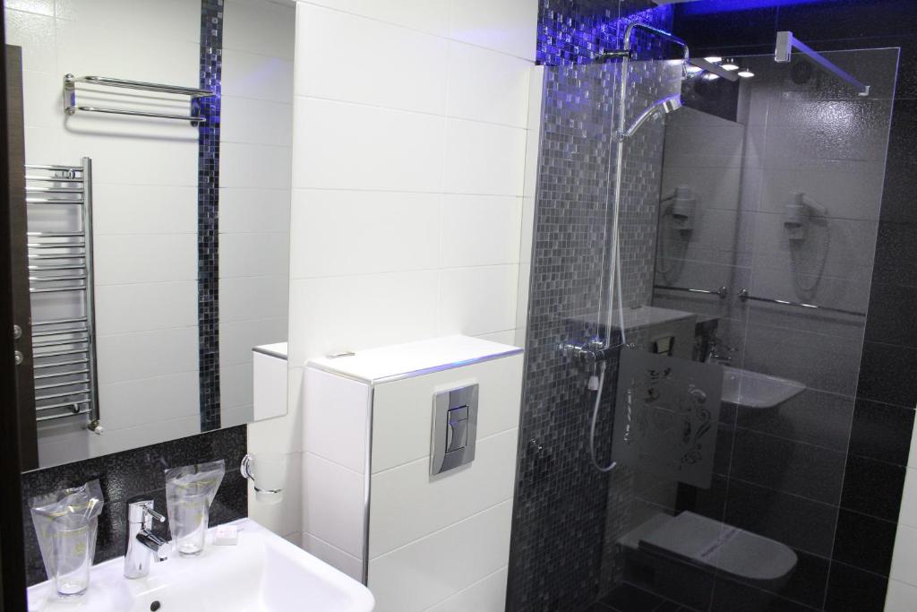 Glass-enclosed shower with blue mosaic accent, wall-mounted toilet, heated towel rack, sink with toiletries and decorative glass at City Palace Hotel in Ohrid