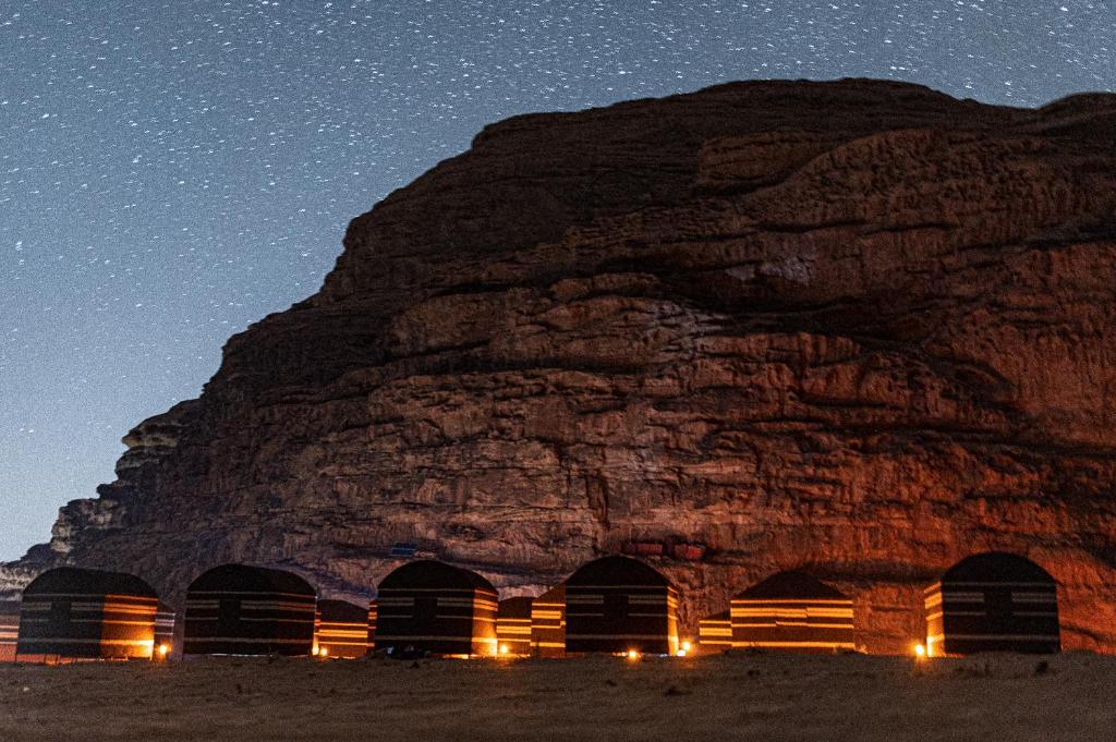 un groupe de cabanes en face d'une montagne la nuit dans l'établissement Wadi Rum Magic Nature Camp, à Wadi Rum