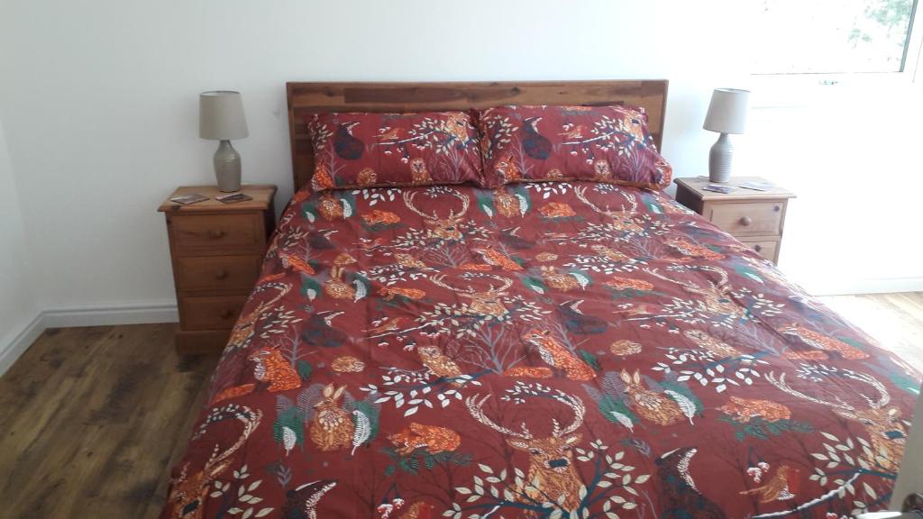 a bedroom with a bed with a red comforter and two lamps at Torgoyle Cottage in Inverness