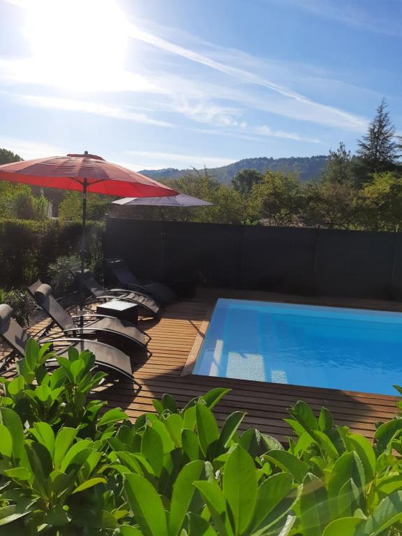 uma piscina com um guarda-sol vermelho e cadeiras ao lado de uma piscina em The Railway Cottage at Montazels em Espéraza