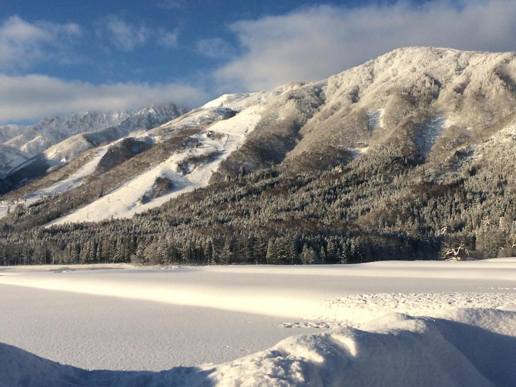 a snow covered mountain with a lake in front of it at Balls Deep Inn Villas in Hakuba