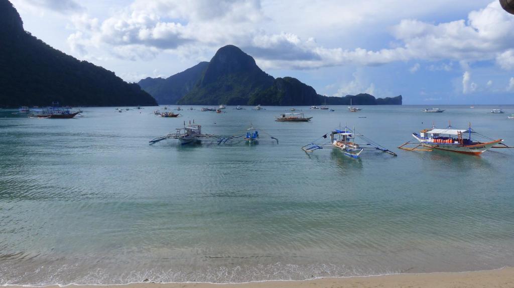 a group of boats in the water near a beach at Bangka Hostels in El Nido