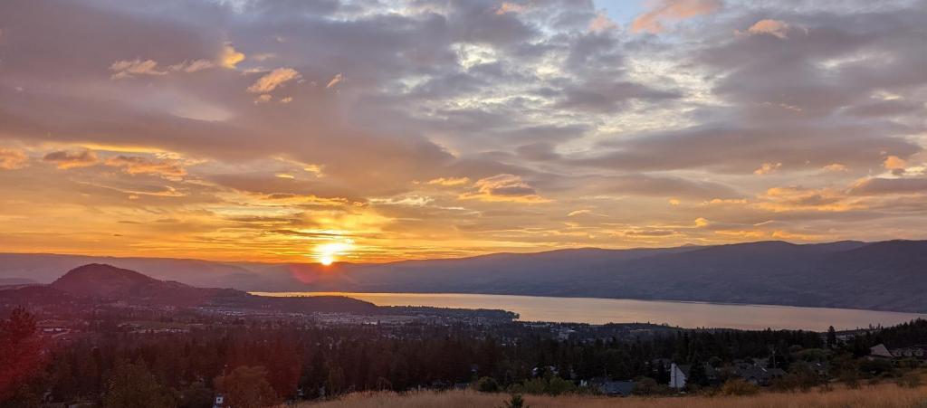 a sunset over a lake with a city and mountains at Autumn Lane, modern Farmhouse Style B&B with Stunning Lakeviews in West Kelowna