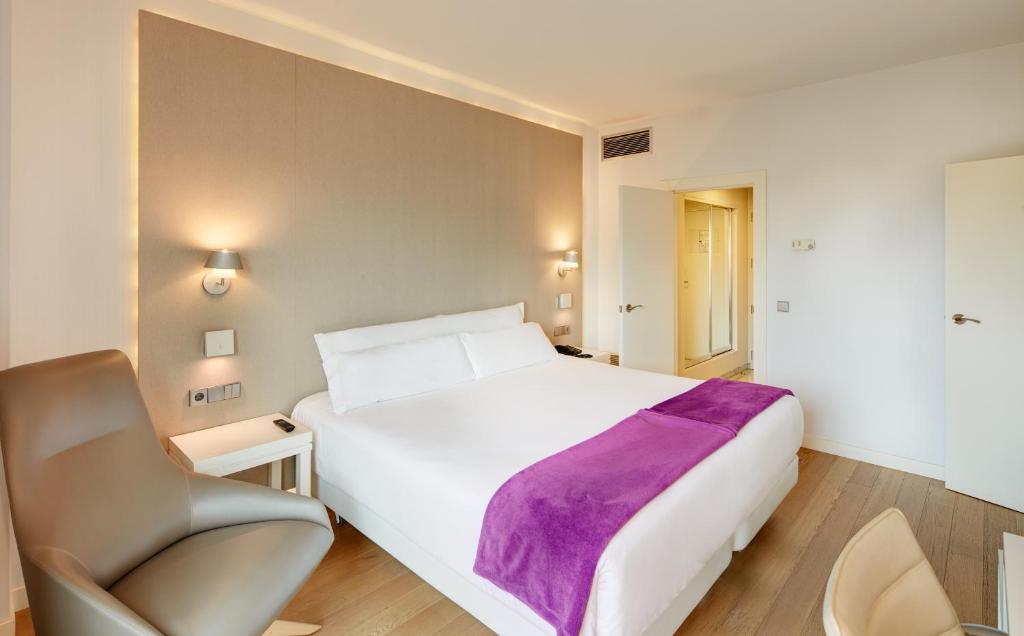 um quarto com uma grande cama branca e uma cadeira em Sercotel Amistad Murcia em Múrcia