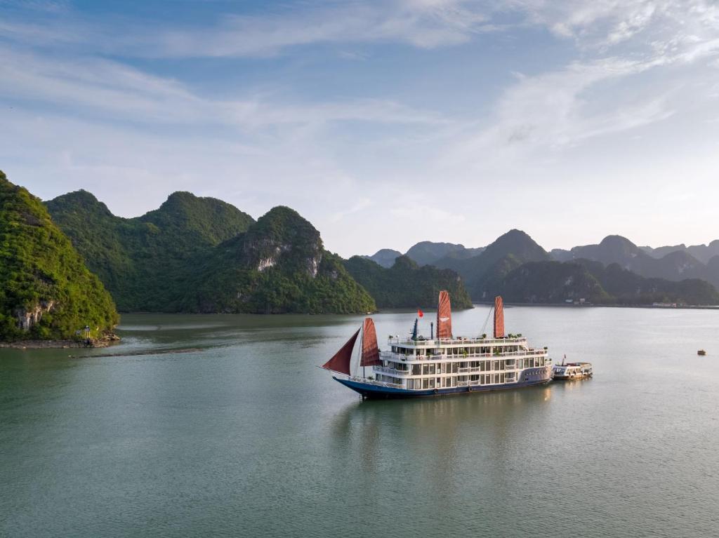 ein Kreuzfahrtschiff auf dem Wasser mit Bergen im Hintergrund in der Unterkunft Verdure Lotus Cruises in Hạ Long