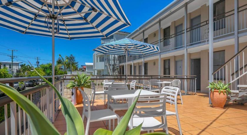 un patio con mesas blancas, sillas y sombrillas en Camden Motor Inn, en Gold Coast