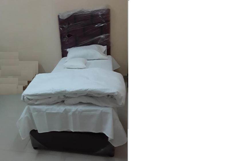 uma cama com lençóis brancos e almofadas num quarto em غرف مجهزة سكن وتجارة عرعر رجال فقط em Arar