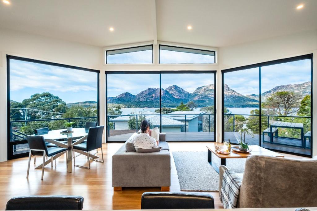a woman sitting on a couch in a living room with large windows at At The Bay in Coles Bay