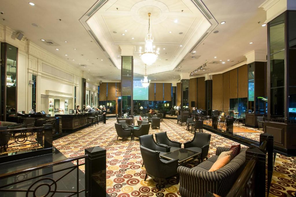 A spacious hotel lobby lounge with chandeliers, patterned carpet, and seating groups around a central area.