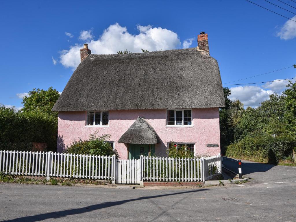 una casa rosa con una cerca blanca delante de ella en Old Cross Cottage, en Whitchurch Canonicorum