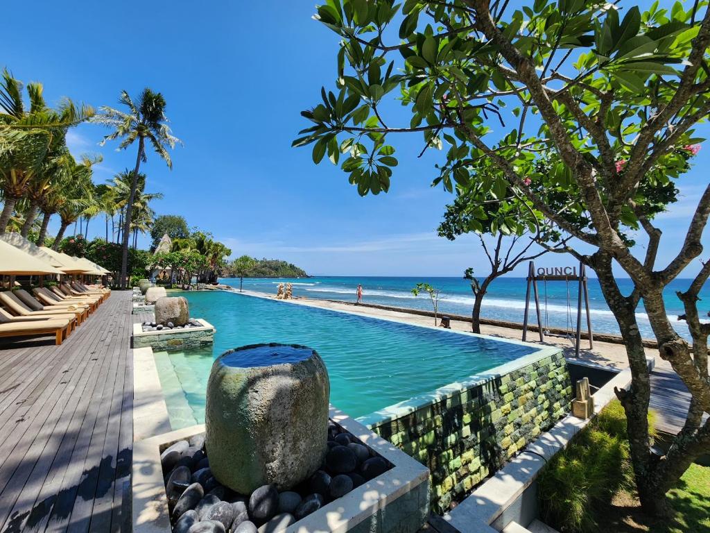 une piscine dans un complexe avec l'océan en arrière-plan dans l'établissement Qunci Villas Resort, à Senggigi