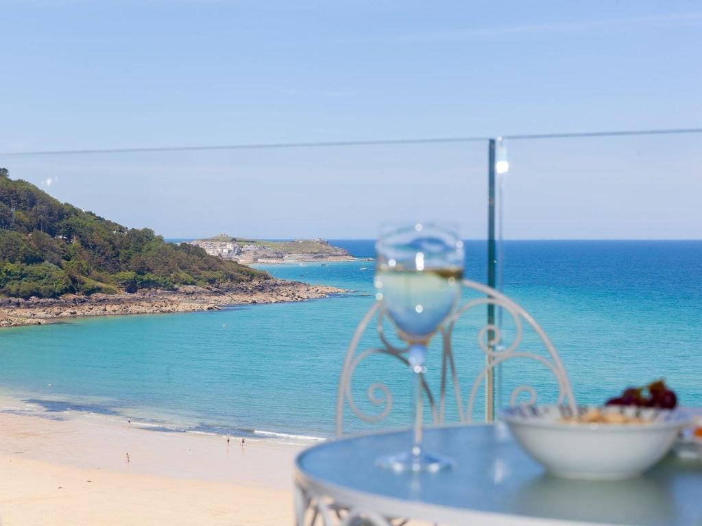 a glass of wine sitting on a table next to a beach at Surf and Sand in St Ives